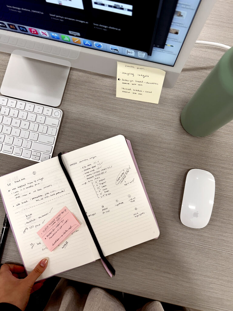desk with sticky notes in a notebook and a computer