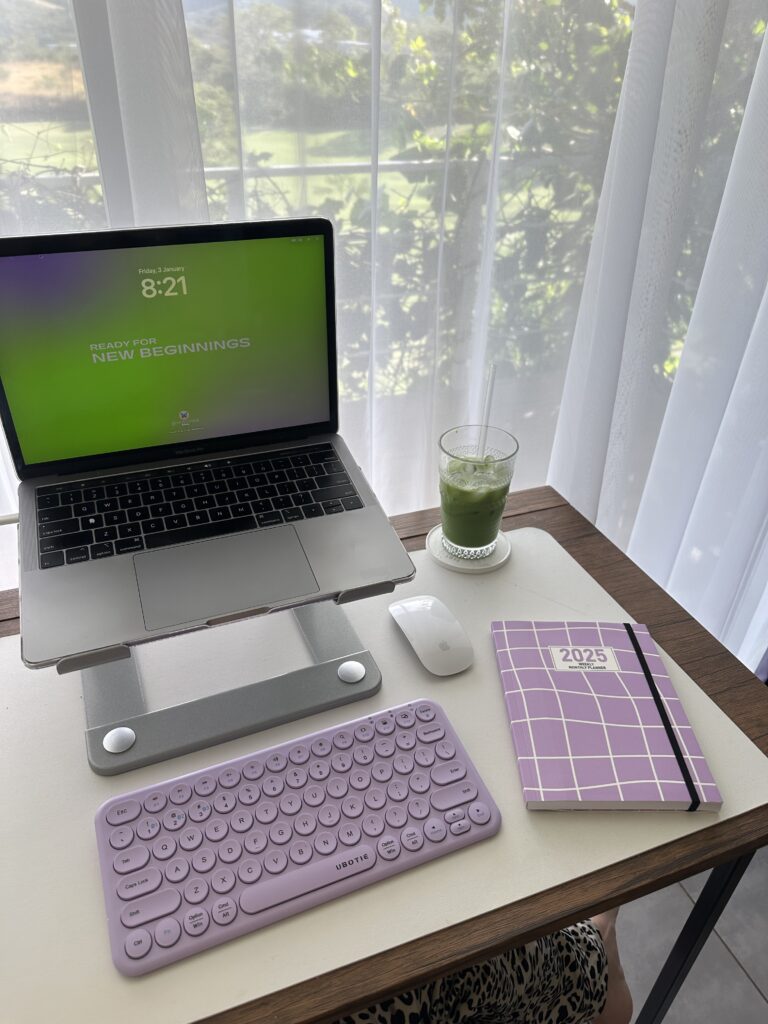 Desk with a computer on a computer stand, a separate keyboard, a mouse, a planner, and a glass of matcha